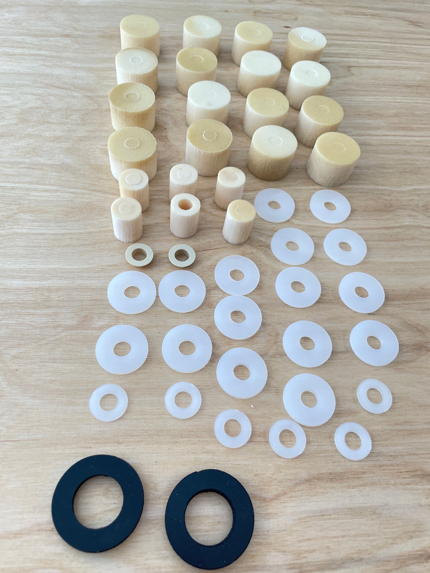 A complete set of elastomers, spacers, and end stops for a Votec GS4 suspension fork, suitable for a rider weight of 100 kg, neatly arranged on a wooden surface. The elastomers and washers are sorted by size and function.