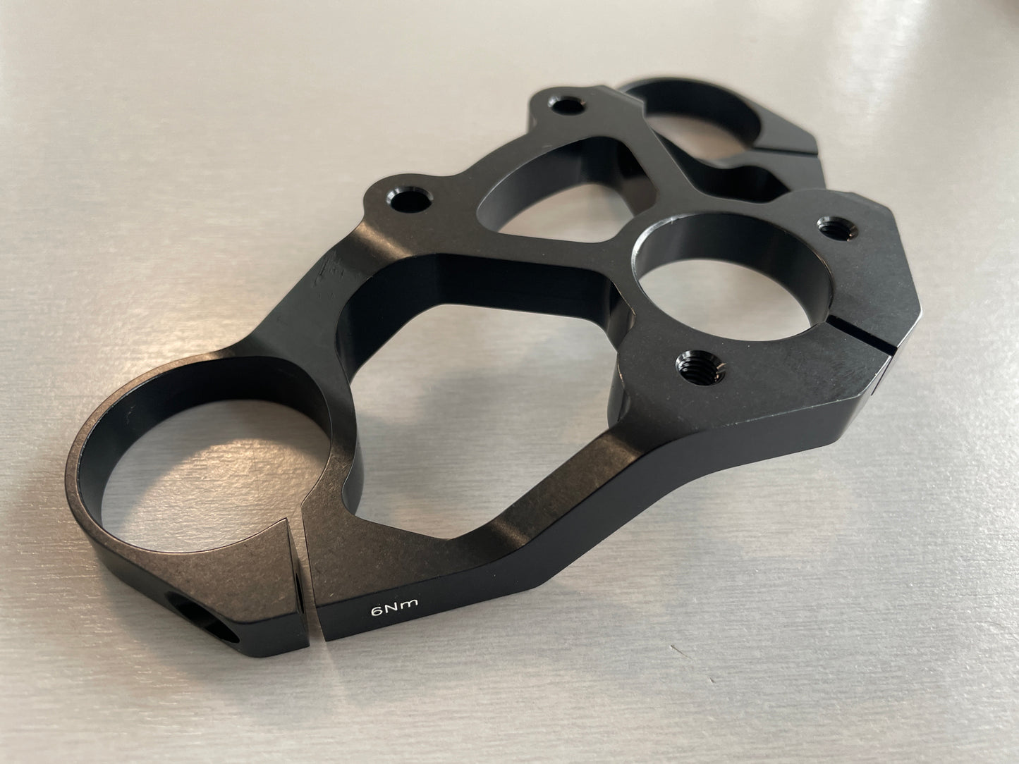 A curved fork crown bridge from Votec made of aluminum. The bridge is slightly bent in shape and serves to attach the fork legs to the bicycle frame.